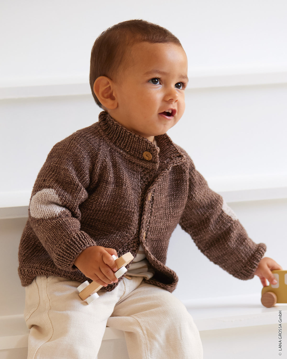 Babyjakke i Cool Wool Big fra Lana Grossa med raglan og kontrastfarvede albuelapper