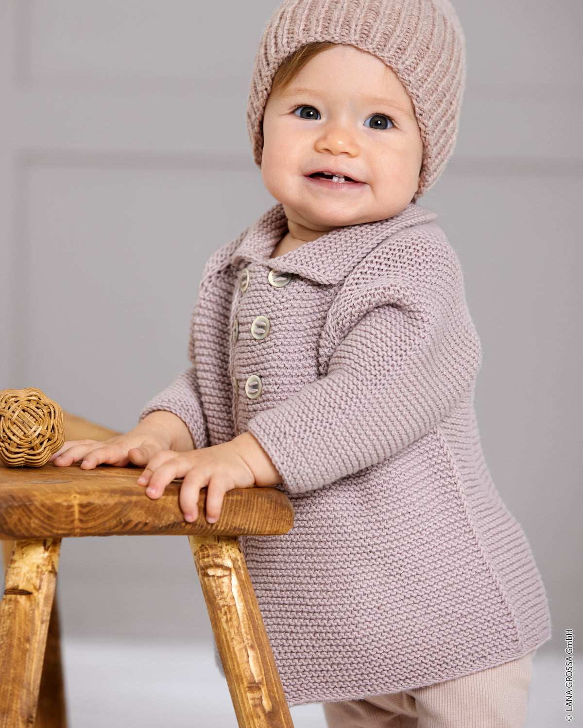 Baby i strikket frakke med krave, raglanærmer og dobbeltradet knaplukning i Cool Wool Big fra Lana Grossa i farven Rosentræ (953).